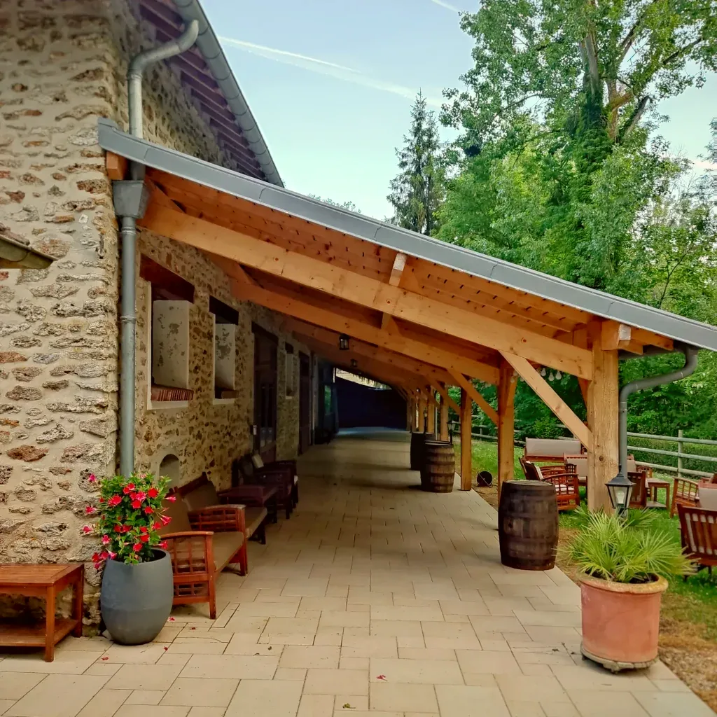 Galerie couverte en bois et tonneaux décoratifs le long de la salle de réception du Moulin Bicheret